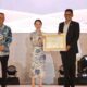 Li Claudia Chandra menyerahkan piagam penghargaan kepada Muhammad Kamaluddin disaksikan Amsakar Achmad.