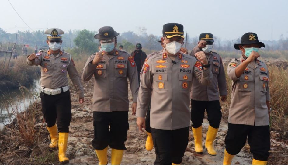 Kapolres Lingga dan petugas kepolisian menyiram sisa bara kebakaran lahan gambut di Singkep Barat yang berjarak 500 meter dari rumah warga